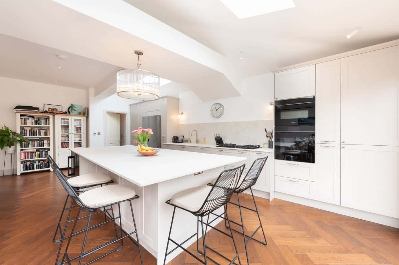 Ebstone Mackintosh kitchen in white with large central island, wire bar stools and herringbone parquet flooring, West London
