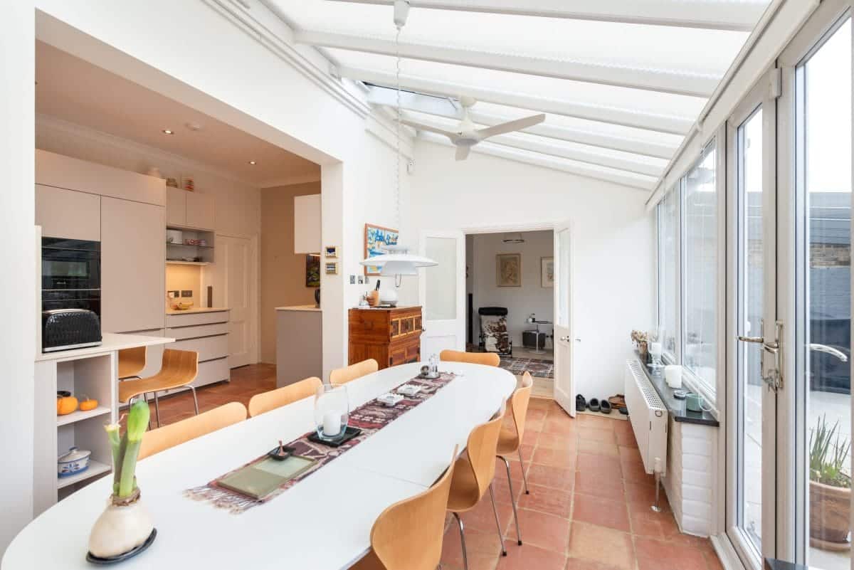 Ebstone Mackintosh white kitchen viewed through archway into conservatory dining room with terracotta tile floor
