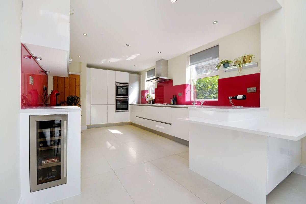 White contemporary kitchen with red glass splashbacks, peninsula and integrated wine cooler.
