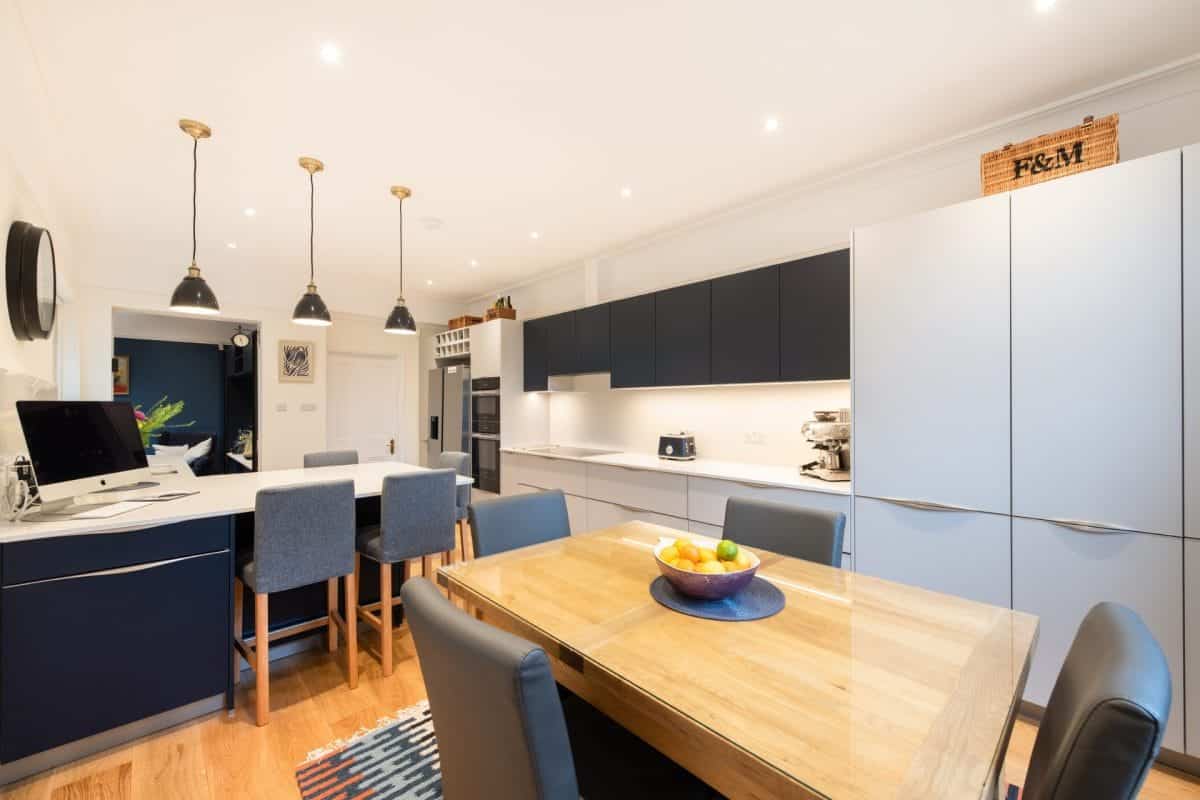 Ebstone navy and pale blue handleless kitchen with brass pendant lights, white worktops and open-plan dining area in Wimbledon