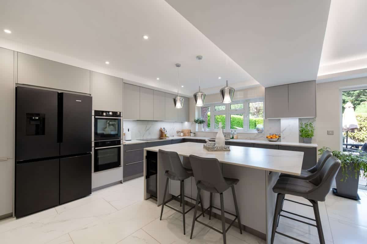 Grey modern kitchen with integrated ovens, large island and black fridge freezer