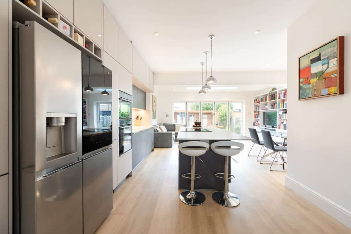 Ebstone grey and white open-plan handleless kitchen with American fridge freezer, island bar stools and garden-facing glazed extension