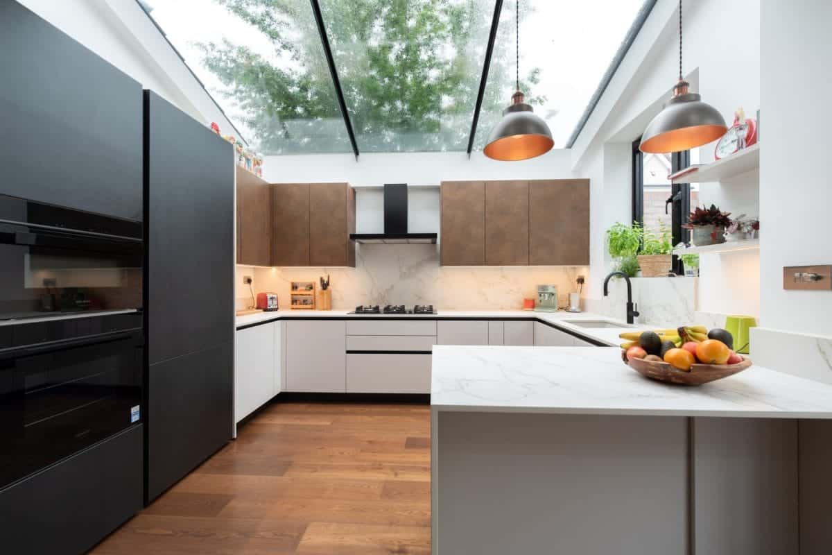 Modern U-shaped kitchen with black appliances, wood-effect cabinets and a glazed roof.