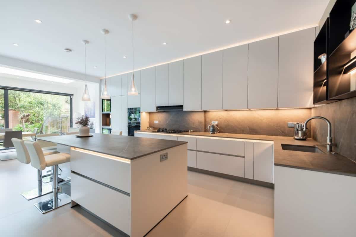 White handleless kitchen with large island, integrated lighting and garden views.