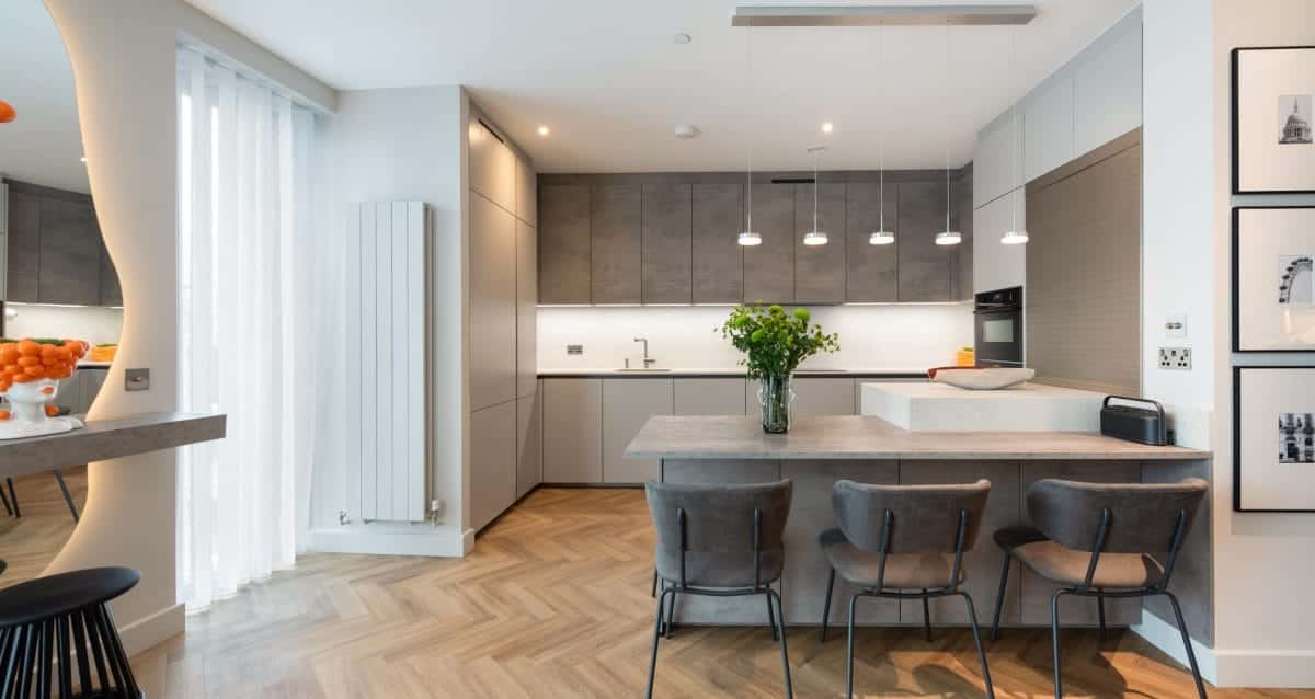 Contemporary grey kitchen with breakfast bar, pendant lights and herringbone wood flooring.