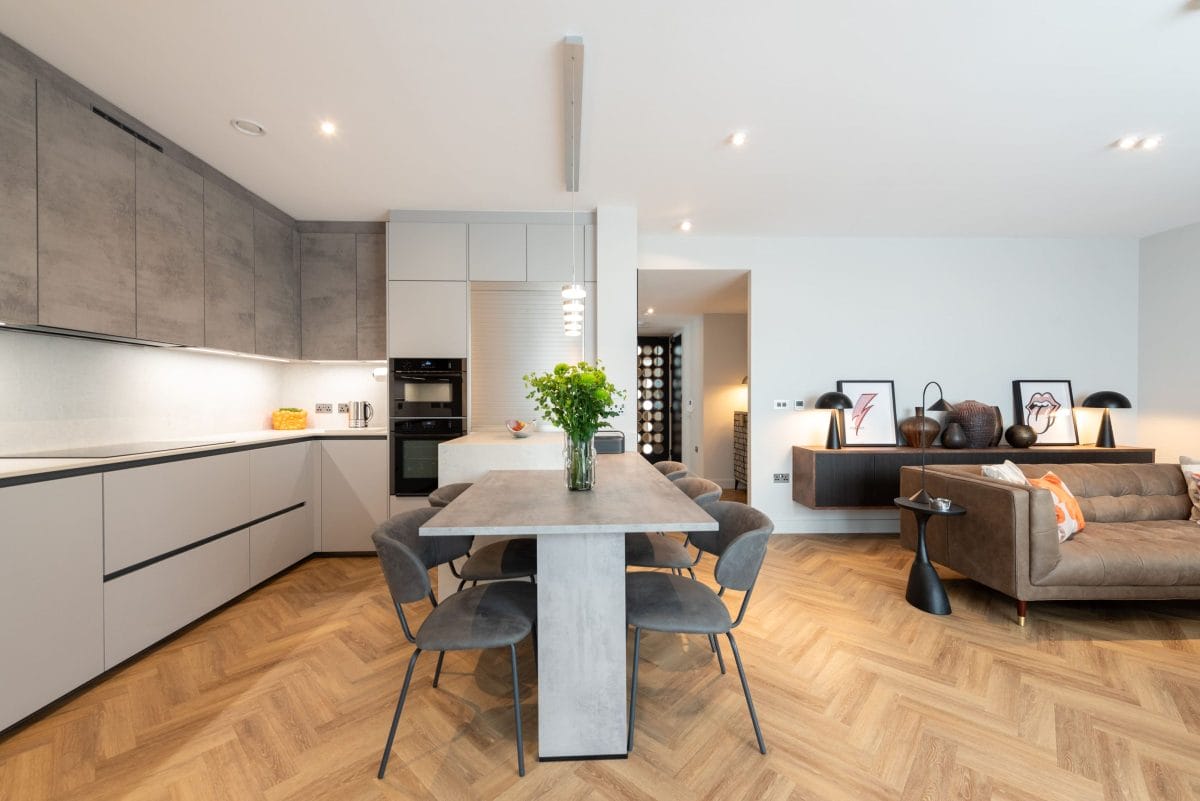 Contemporary open-plan German kitchen with island dining table and grey handleless units by Ebstone Kitchens