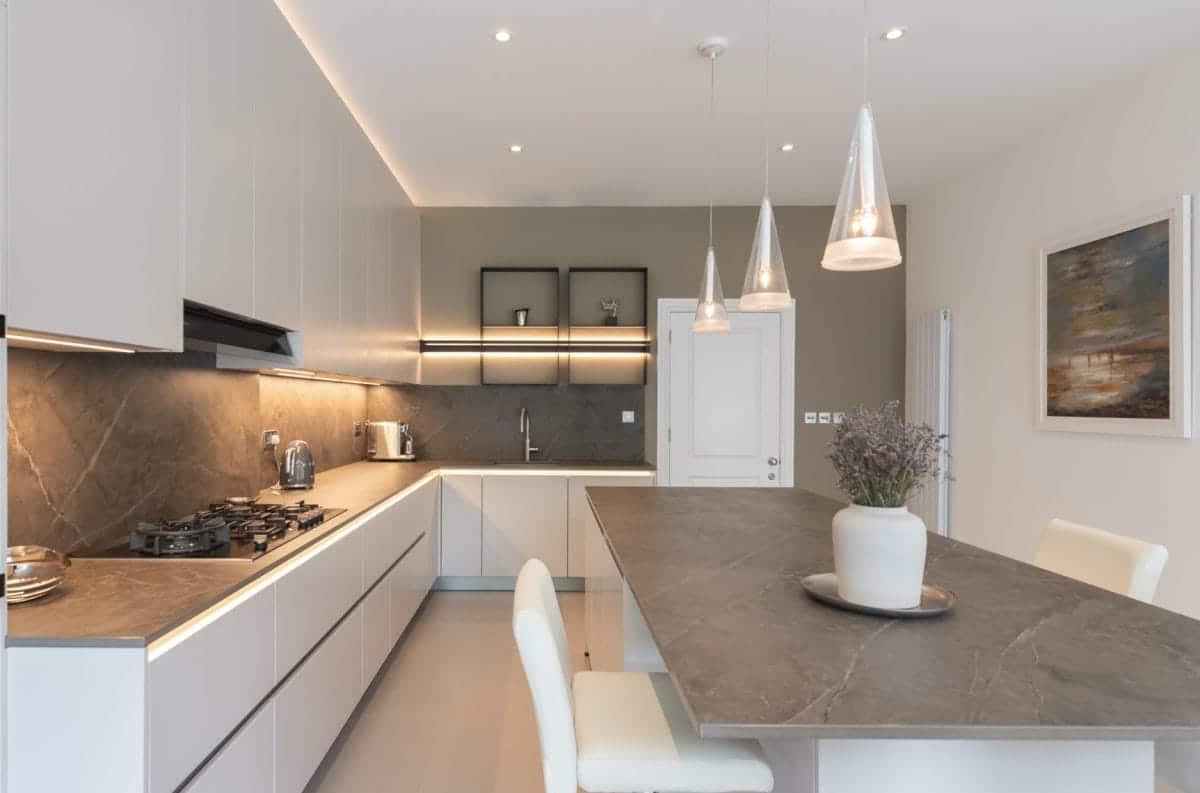 Ebstone Mackintosh kitchen with white handleless cabinetry, stone effect worktop and splashback, and glass cone pendant lights