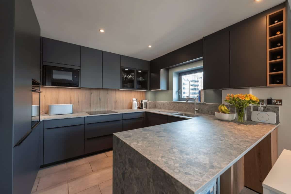 Modern dark kitchen with textured grey worktops, wood accents, integrated appliances and open wine storage