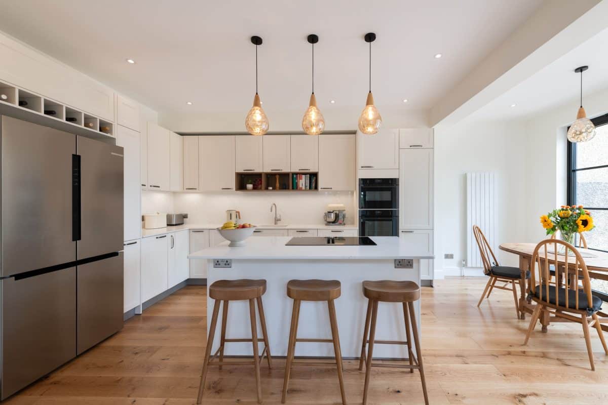 Open-plan white kitchen with integrated oven, island seating and freestanding fridge freezer