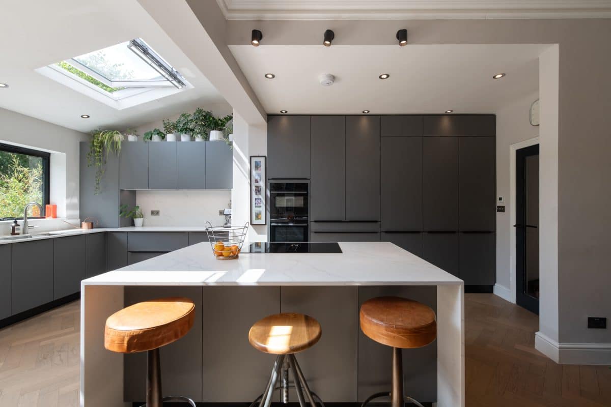 Dark grey handleless kitchen with white island, wooden stools and rooflight